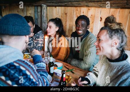 Portrait of young man sitting with friends talking while having food in log cabin Stock Photo