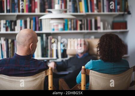 Mature couple discussing with therapist while sitting against bookshelf Stock Photo