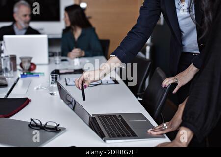 Midsection of businesswomen discussing over laptop with colleagues working in background at office Stock Photo