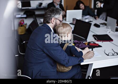 Businessman with son working at conference table while colleagues in background Stock Photo
