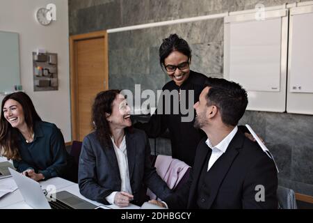 Smiling businesswoman interacting with cheerful colleagues in office Stock Photo