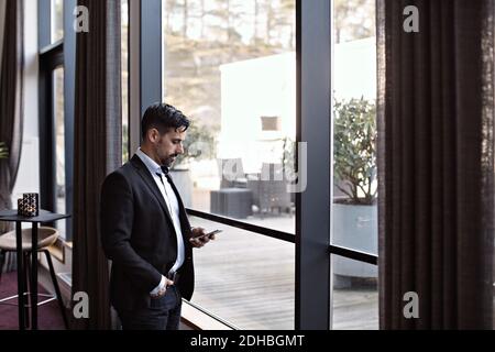 Businessman using phone while standing by window in office Stock Photo