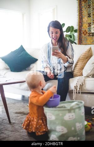 Happy working mother photographing playing daughter while telecommuting in living room Stock Photo