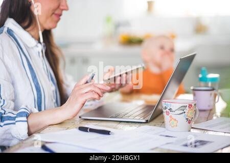 Midsection of working mother using technologies while daughter sitting in background at dining table Stock Photo
