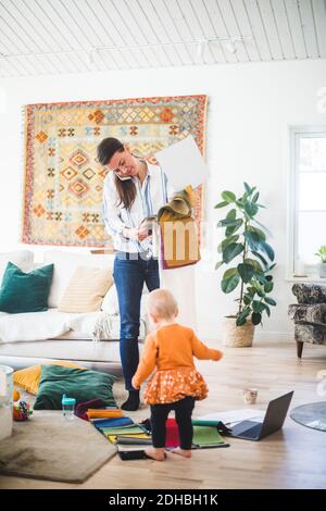 Busy freelancing designer answering smart phone while holding fabric swatch by daughter in living room at home office Stock Photo