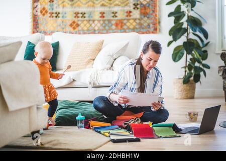 Fashion designer examining papers while daughter playing in living room Stock Photo