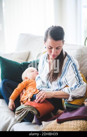 Working mother with sleeping daughter and fabric swatch sitting on sofa at home Stock Photo