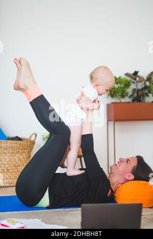 Side view of cheerful mother playing with daughter while lying in home office Stock Photo
