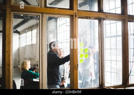 Male IT professional discussing plan with businesswoman over adhesive notes seen through glass in office Stock Photo