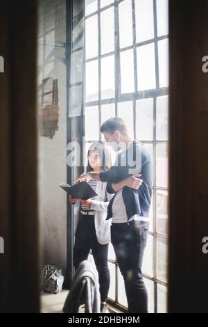 Male computer programmer discussing over work diary with coworker seen through glass wall at creative workplace Stock Photo