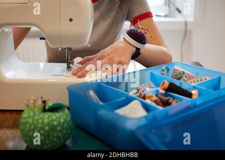 Midsection of tailor using sewing machine by blue box at table Stock Photo