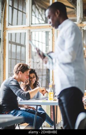 Smiling computer programmers using laptop while businessman standing in foreground at creative office Stock Photo