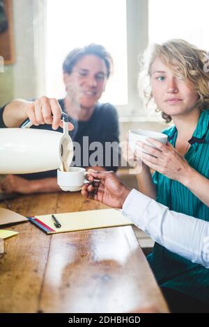 Male computer programmer serving hot coffee to colleague at desk in office Stock Photo