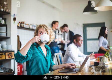 Young businesswoman drinking coffee while computer programmers working in background at office Stock Photo