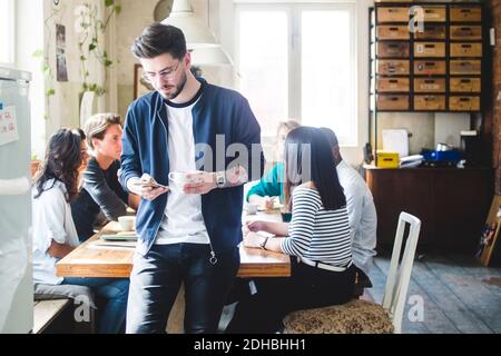 Young male professional using smart phone while IT programmers having meeting at desk in office Stock Photo