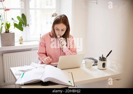 Female accountant using laptop while doing paperwork at home Stock Photo