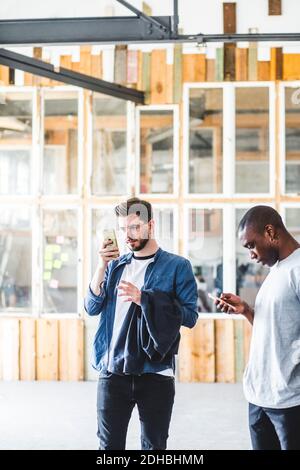 Serious young male IT experts using smart phones while standing in office Stock Photo