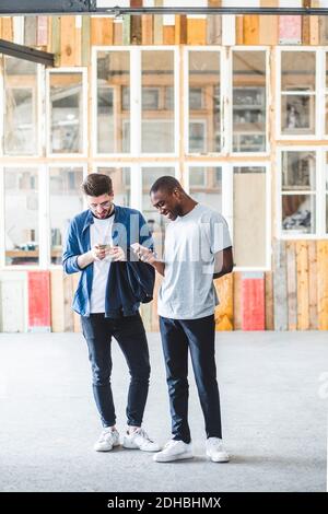 Full length of smiling businessmen text messaging using mobile phones at creative workplace Stock Photo