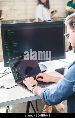 Male computer programmer coding in laptop while working at desk in office Stock Photo
