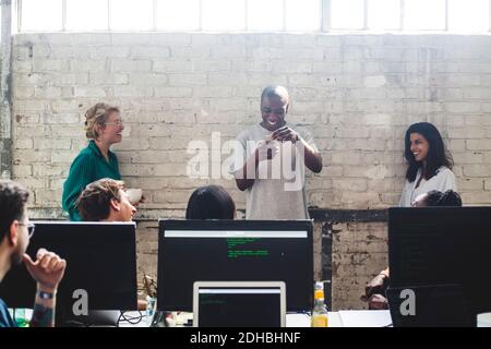 Smiling young colleagues looking at male programmer using smart phone against wall in office Stock Photo