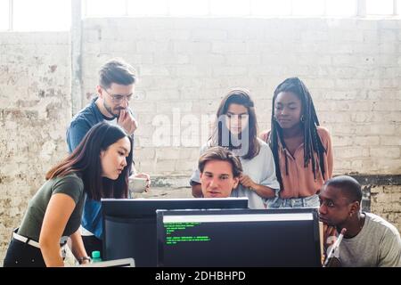 Serious computer programmers looking at computer monitor while brainstorming at workplace Stock Photo