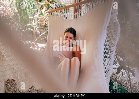 Smiling mature woman using digital tablet in hammock at beach Stock Photo