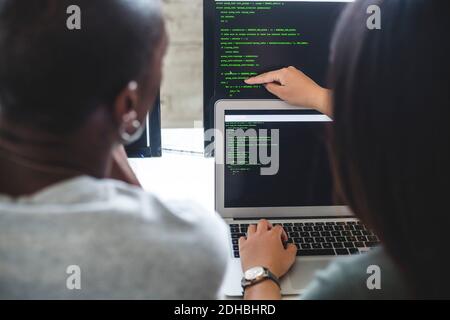 Rear view of female entrepreneur pointing at codes on computer monitor to male hacker in office Stock Photo