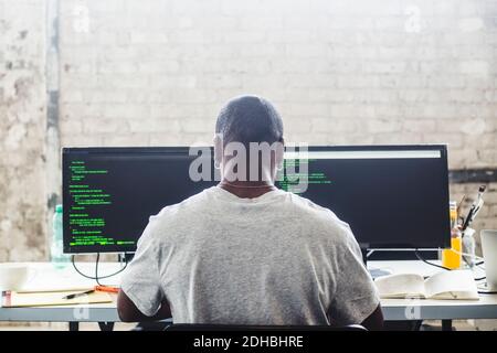 Rear view of male IT expert using computer while coding at creative workplace Stock Photo