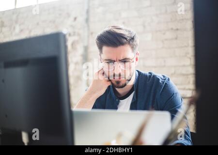 Male IT professional thinking while working on computer codes in laptop at workplace Stock Photo