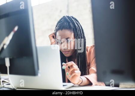 Serious female IT expert concentrating on computer codes while using laptop at workplace Stock Photo
