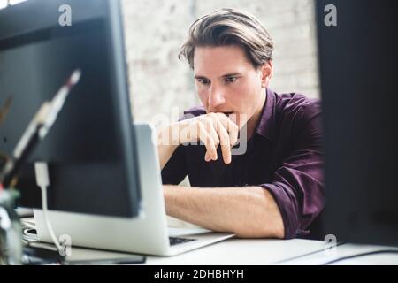 Serious male IT professional thinking while coding in laptop at creative workplace Stock Photo