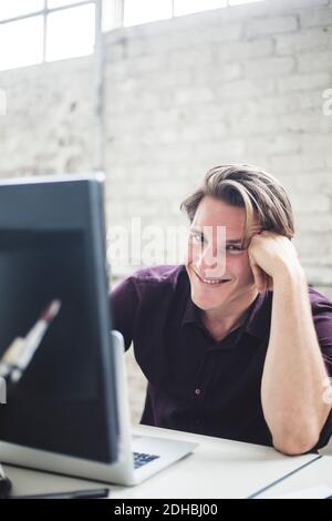 Portrait of smiling young male programmer coding at desk in office Stock Photo