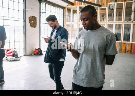 Confident young businessman using smart phone while walking by colleague at creative workplace Stock Photo