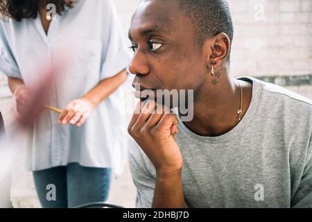 Thoughtful young male hacker looking away while sitting with hand on chin at workplace Stock Photo