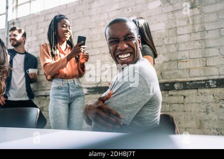 Cheerful young male hacker looking over shoulder while sitting in board room at creative office Stock Photo
