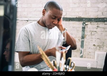 Young male hacker using smart phone while sitting at creative workplace Stock Photo