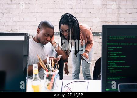 Young businesswoman looking at businessman using smart phone in creative office Stock Photo