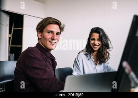 Portrait of confident male and female IT professionals sitting at desk in creative office Stock Photo