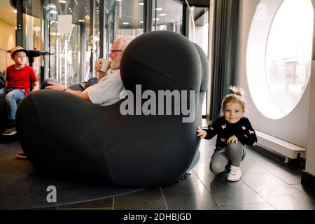 Portrait of smiling girl hiding by armchair in hotel lobby Stock Photo