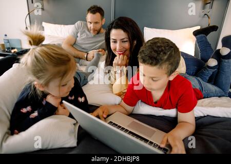 Parents and girl with boy using laptop on bed in hotel room Stock Photo