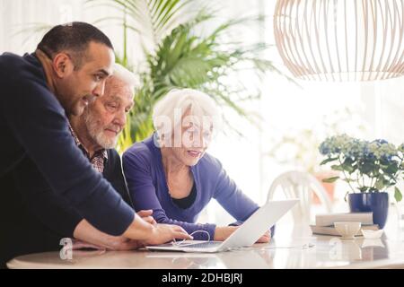 Mature man using laptop with parents at table in nursing home Stock Photo