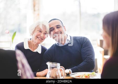 Smiling senior woman sitting with son while having lunch at table in nursing home Stock Photo