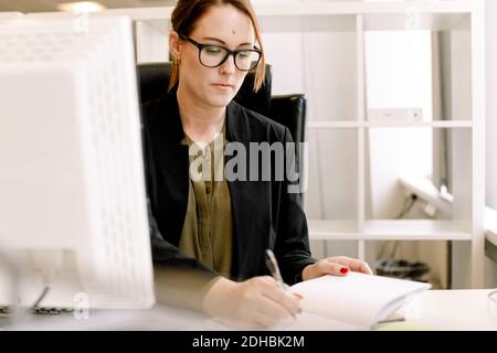 Mid adult female sales manager writing on book at desk in office Stock Photo