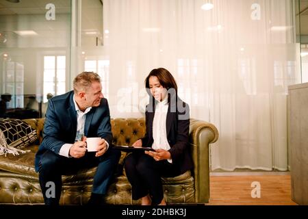 Sales professionals discussing over digital tablet while sitting on sofa at work place Stock Photo