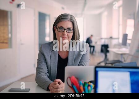 Portrait of confident mature businesswoman sitting at desk in office Stock Photo