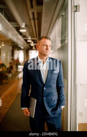 Thoughtful well-dressed mature sales manager looking away while standing in office corridor Stock Photo