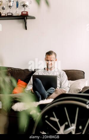 Disabled mature man using laptop while sitting on sofa at home Stock Photo