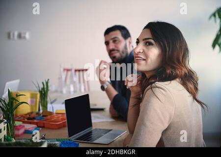 Female and male engineers looking away while sitting at table in office Stock Photo