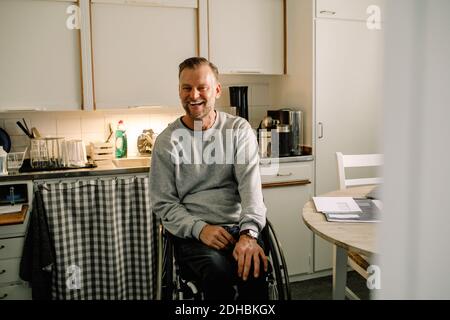 Cheerful mature man sitting on wheelchair in kitchen at home Stock Photo