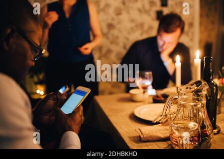 Mature man using mobile phone while having dinner with friends at party Stock Photo